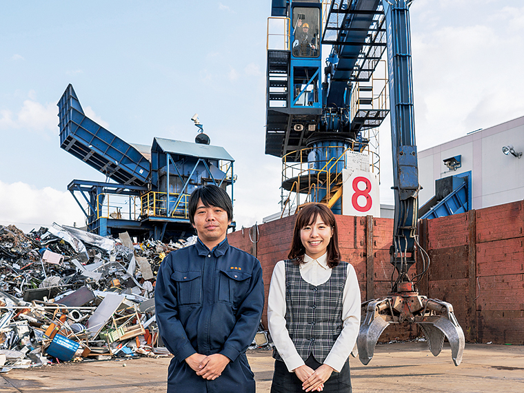 廃棄物を破砕機へと運ぶ巨大なタワークレーンの前に立つ橋本雅人さんと八木沼楓さん