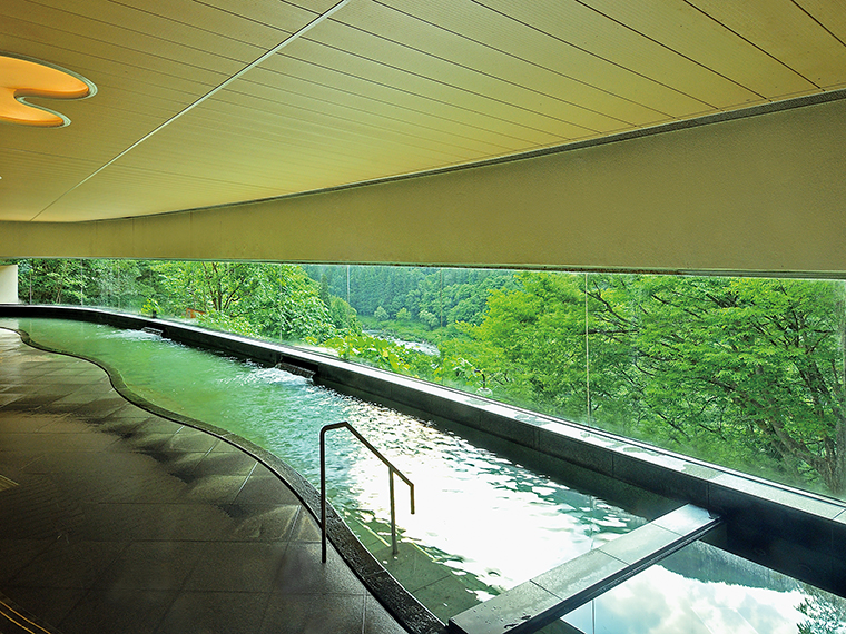 本館の「渓流展望風呂」。長さ30mに及ぶ総ガラス張りで、渓谷麓の大川（阿賀川）まで山渓を一望できる