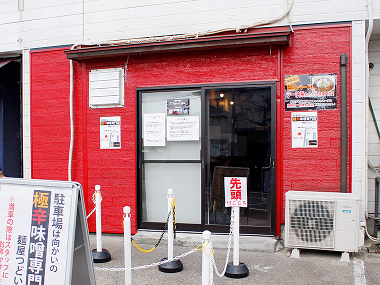 「麺屋つどい」の道路を挟んだ向かいにある、赤い外観の店舗。駐車の際は「麺屋つどい」の駐車場を利用しよう