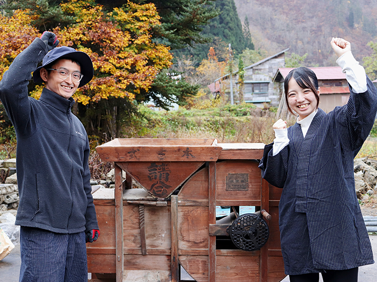 2人の後ろにある大きな農機は、大豆の選別を行う唐箕（とうみ）。風を送り、重さで選別する仕組み