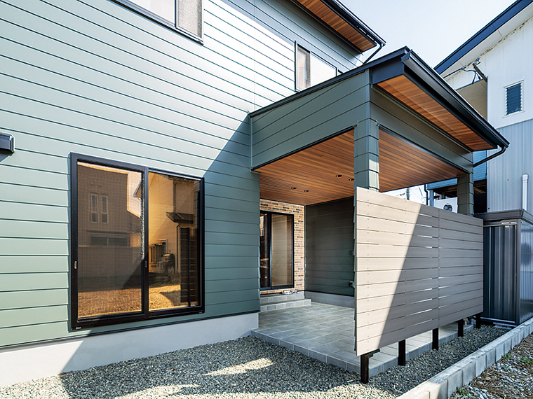 アウトドアリビングにくすみカラーの人工木フェンスと物置を配置